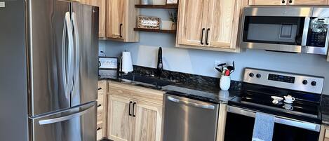 A modern kitchen with stainless steel appliances, wooden cabinets, and a granite countertop.