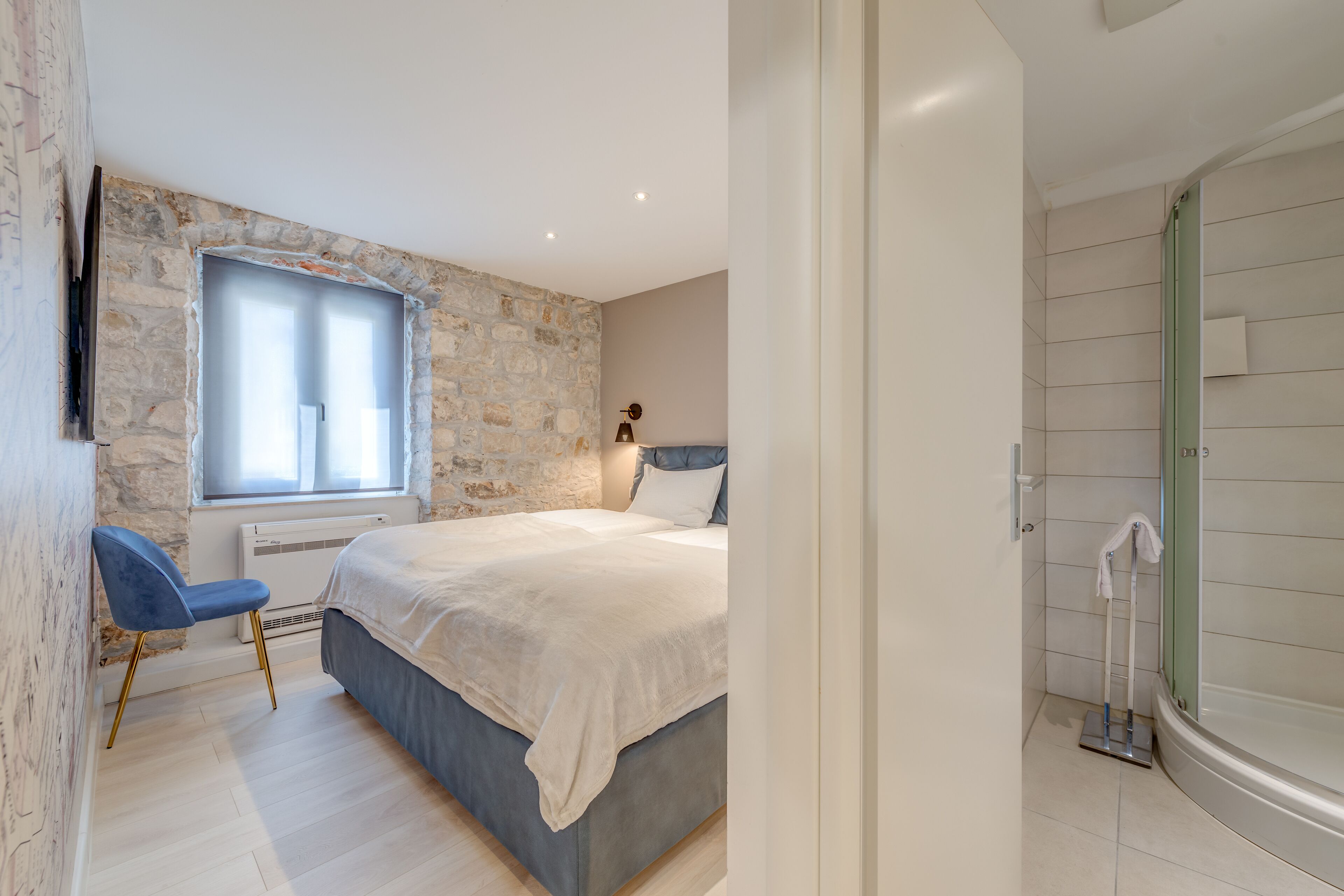 A bedroom with a stone wall, a bed, a window, a chair, and a shower area.