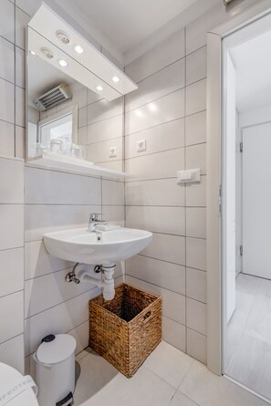 Un baño moderno con un lavamanos blanco, un espejo y piso de baldosas.