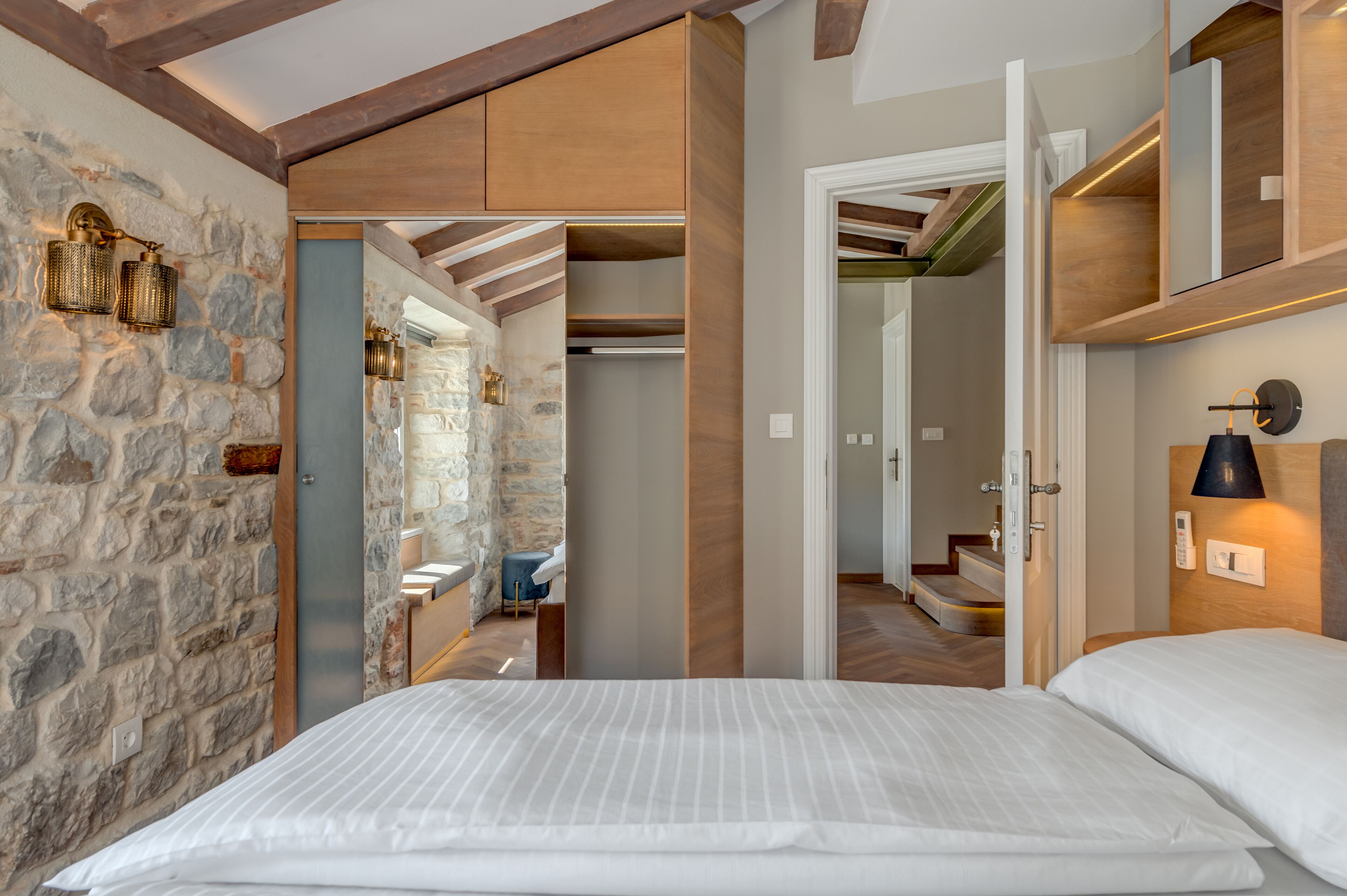 A bedroom with a stone wall, wooden beams, a bed, and a wardrobe.