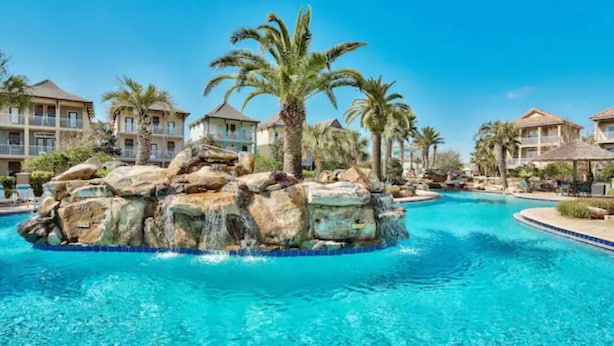 Ein Pool mit einer Felseninsel und Palmen, umgeben von Hotelgebäuden.