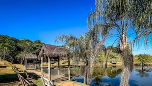 A thatched-roof pavilion, a wooden fence, and a body of water in a park setting. - Vale Das Aguas Thermas Park (Piracicaba)