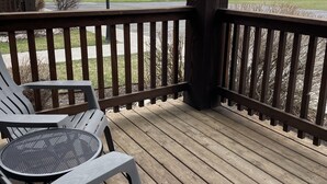 A wooden deck with two Adirondack chairs and a table, overlooking a grassy field and distant mountains. - Buffalo Valley - Spacious Condo w/ 1 king bed and 2 queen beds (Driggs)