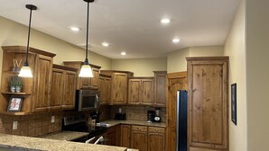 A kitchen with wooden cabinets, granite countertops, stainless steel appliances, and pendant lighting. - Buffalo Valley - Spacious Condo w/ 1 king bed and 2 queen beds (Driggs)