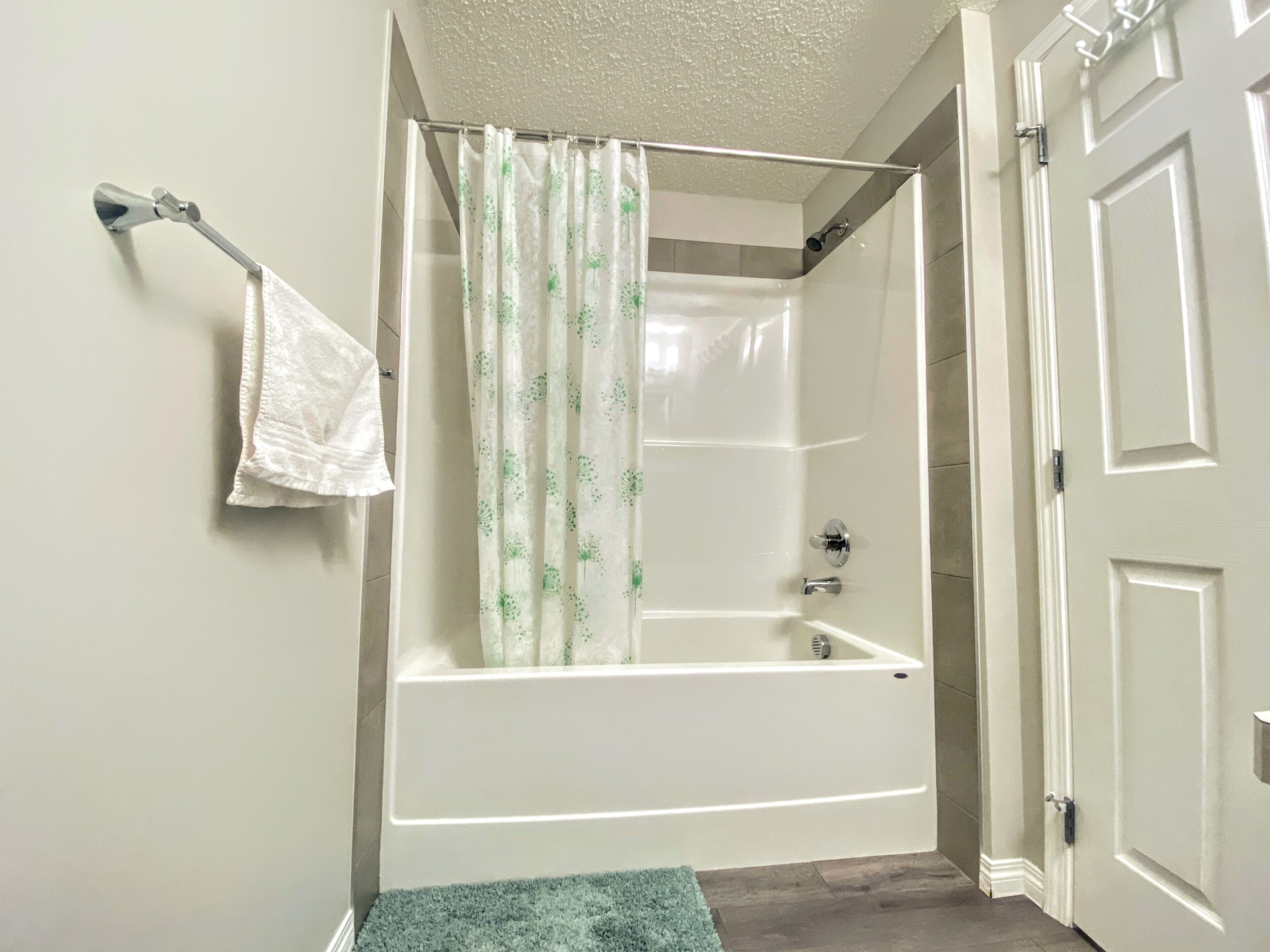 A bathroom with a bathtub, shower curtain, and a towel rack.
