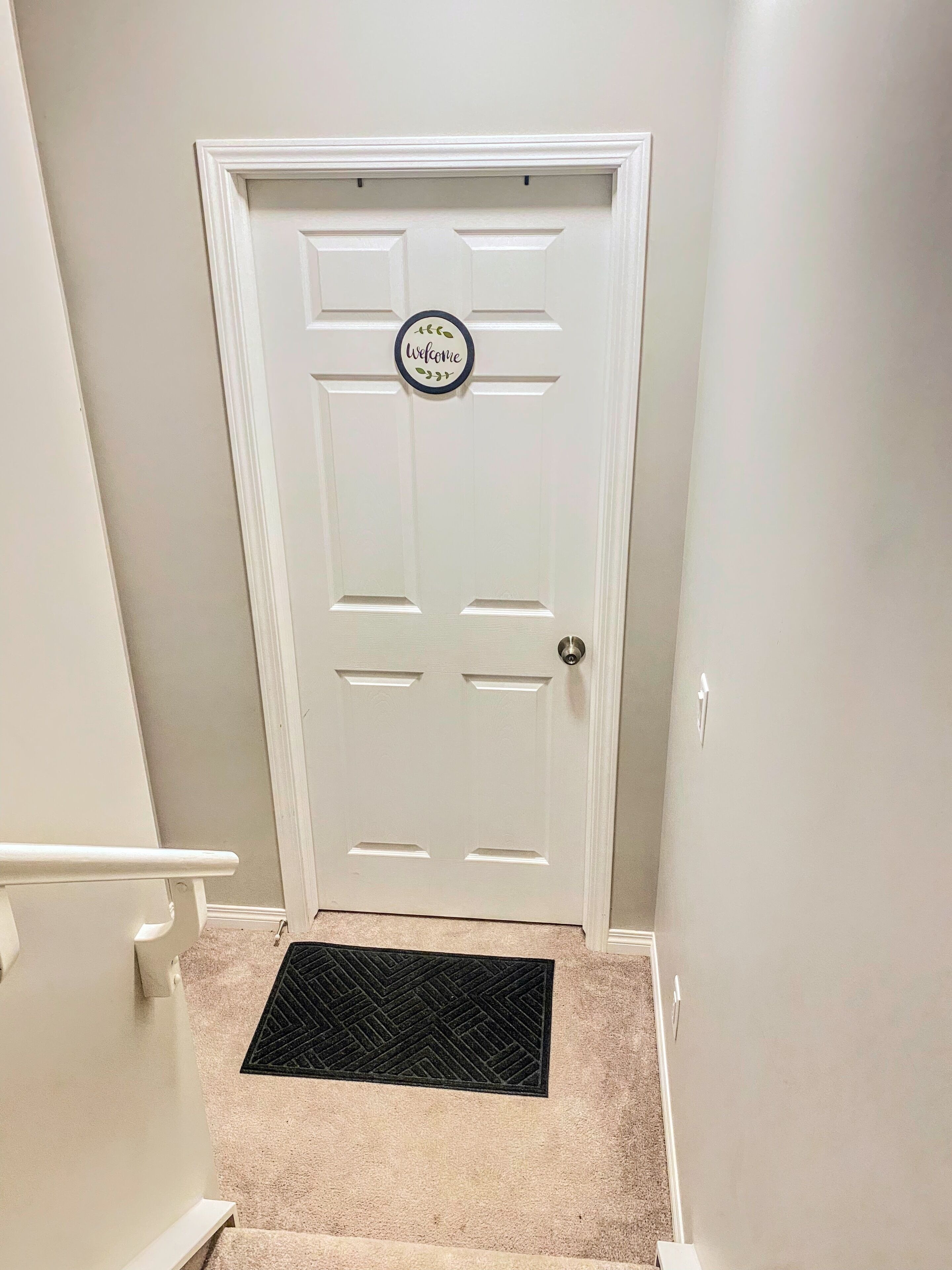 A white door with a 'Welcome' sign, a black doormat, and a white handrail.