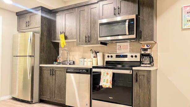 A modern kitchen with dark wood cabinets, stainless steel appliances, and a tiled backsplash. - Newly Built and Cheerful 1-Bedroom Suite (Calgary)
