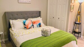 A neatly made bed with a green blanket, a white headboard, and a wall-mounted painting of a horse. - Newly Built and Cheerful 1-Bedroom Suite (Calgary)
