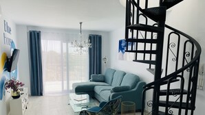 Een moderne woonkamer met een blauwgroene bank, een glazen salontafel, een blauwe fauteuil, een zwart spiraaltrap en een kroonluchter.