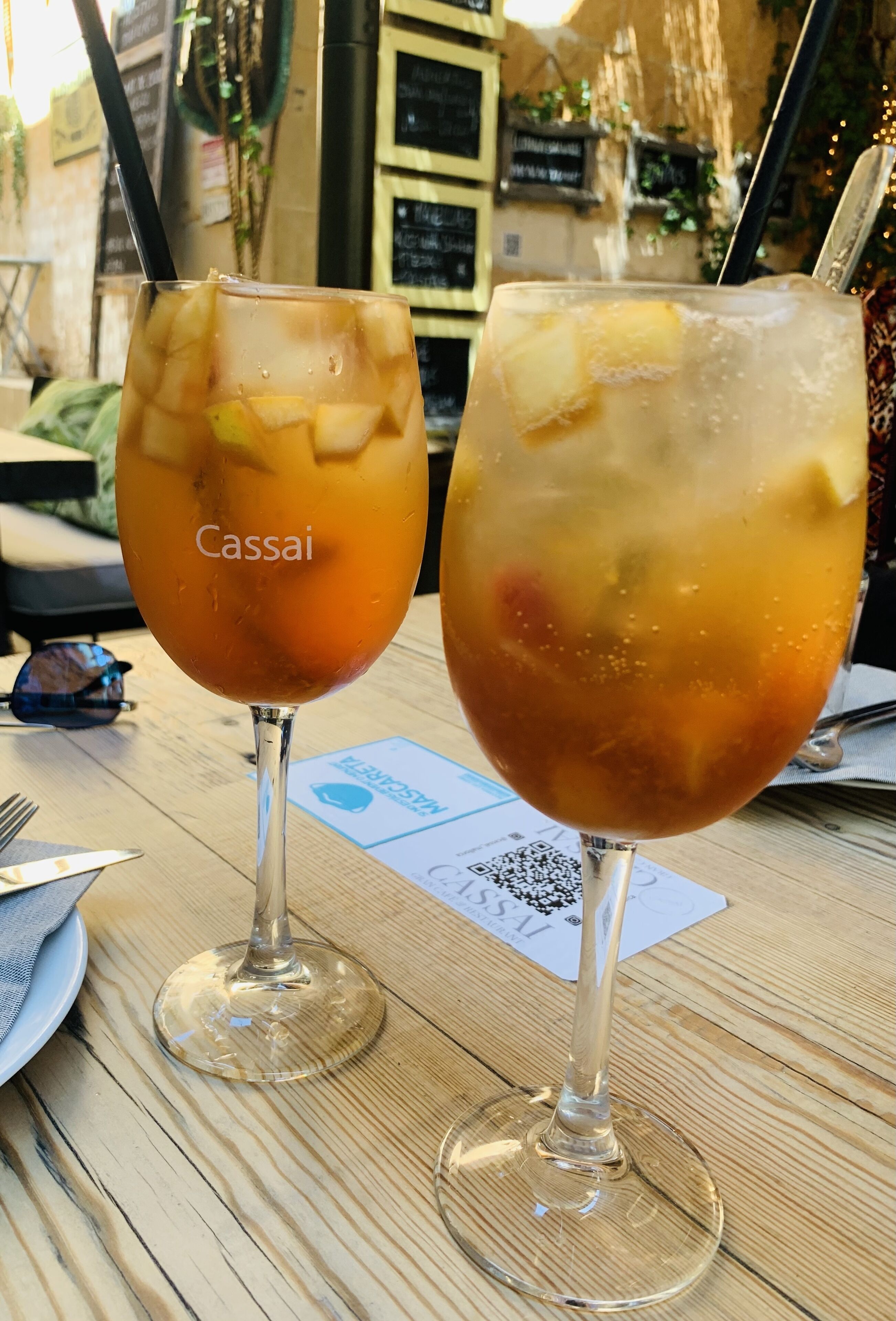 Two glasses of iced beverages on a wooden table with a QR code and a menu.