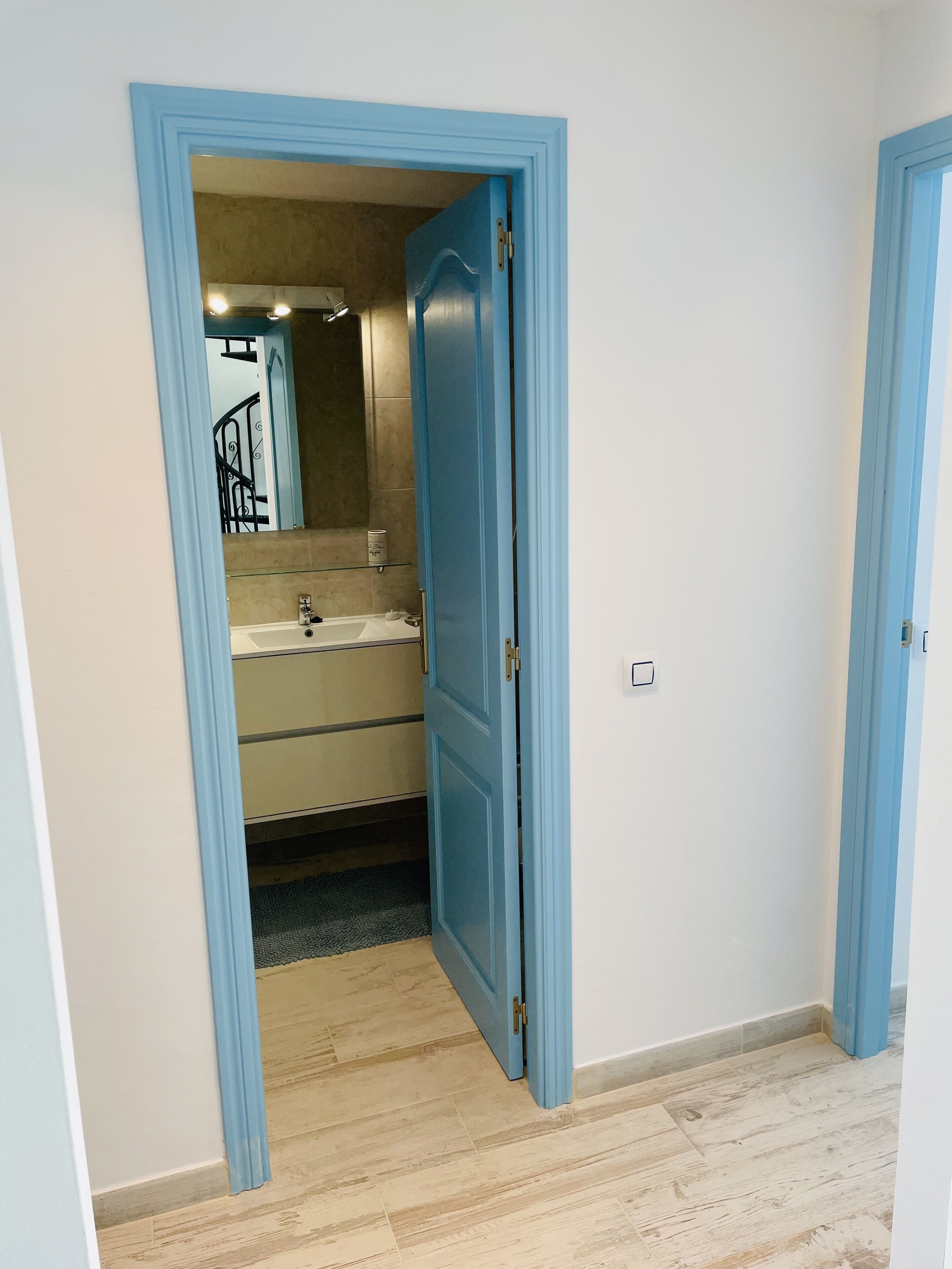 A bathroom with a sink and mirror, a shower, and a door leading to another room.
