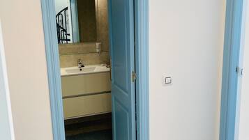 A bathroom with a sink and mirror, a shower, and a door leading to another room.