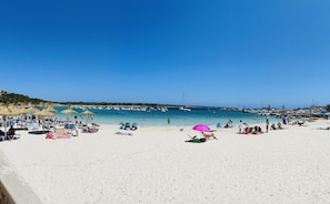 A beach with sun loungers and umbrellas, boats in the water, and a clear blue sky.