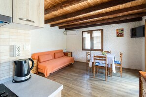 A cozy room with a wooden ceiling, a sofa, a dining table with chairs, and a kettle on the counter.