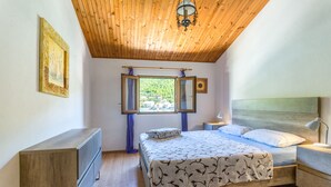 Un dormitorio con techo de madera, una cama con colcha estampada, una mesita de noche con lámpara y una ventana con cortinas.