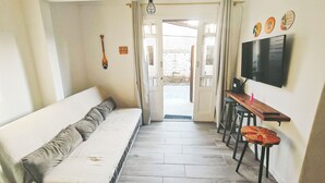 Un couloir avec un canapé, un téléviseur fixé au mur et une porte donnant sur un espace extérieur.