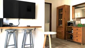Une cuisine compacte équipée d’un téléviseur à écran plat, de deux tabourets de bar, d’un meuble en bois contenant un four à micro-ondes et d’une petite table ronde.