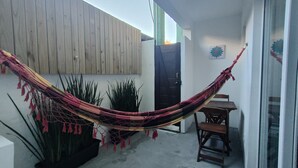 Un hamac tendu entre deux murs, une porte en bois et une petite table avec une chaise.