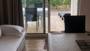 A bedroom with a bed, a desk, and a view through a sliding glass door to an outdoor patio area. - Grapevine Studio Apartment (Zdrelac)