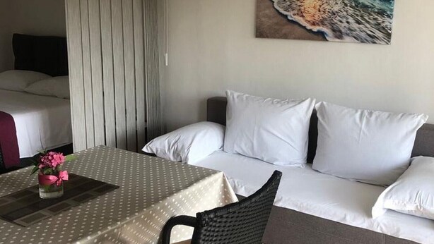 A hotel room with a dining table, a sofa, and a painting of a beach scene. - Grapevine Studio Apartment (Zdrelac)