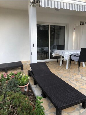 Un patio couvert avec une table et des chaises, un fauteuil et des plantes en pot.