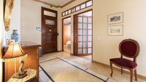 A hotel lobby with a wooden reception desk, a lamp, a chair, a tiled floor, and a door leading to another room. - Ideal 4 bdr Apartment in Plaka for 10! (Athens)