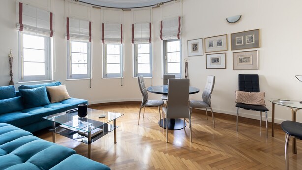 A spacious living room with a blue sofa, a glass coffee table, and a dining area with chairs and a table. - Ideal 4 bdr Apartment in Plaka for 10! (Athens)