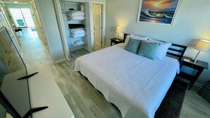 Une chambre d’hôtel avec un lit, deux tables de chevet avec des lampes, un tableau au mur et une armoire contenant des vêtements et des serviettes.