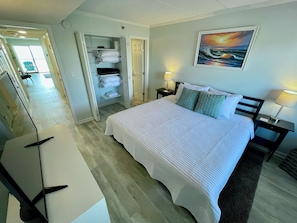 A hotel room with a bed, two bedside tables with lamps, a painting on the wall, and a closet with clothes and towels.