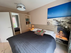 Une chambre à coucher comprenant un lit, une armoire, une table de chevet, une lampe et une fresque murale sur le thème de la plage.
