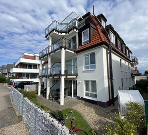 Un immeuble résidentiel à plusieurs étages, doté de balcons, d’un espace extérieur couvert aménagé en coin salon et d’un vélo garé à l’extérieur.