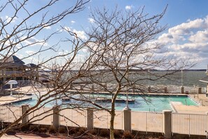 Ein Hotel am Wasserufer mit Pool, Blick auf das Wasser und ein im Vordergrund stehender, kahl stehender Baum.