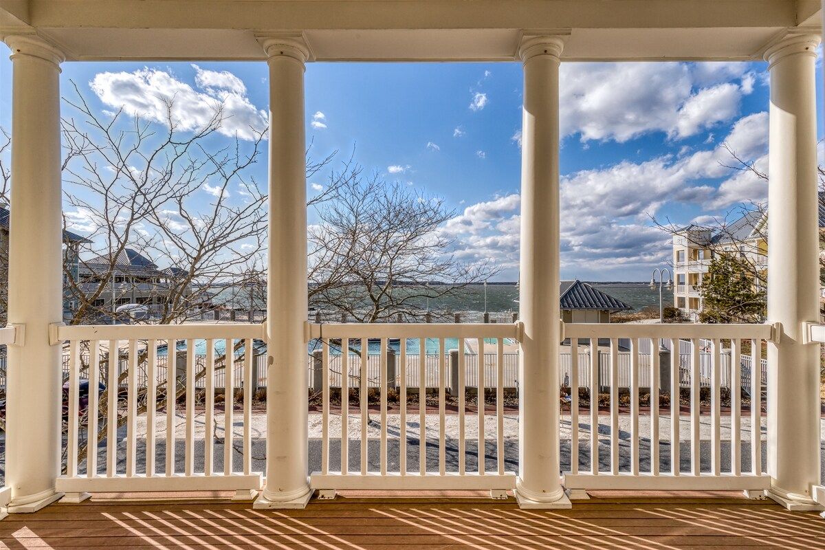 A covered porch with white columns and a view of a beach and buildings.