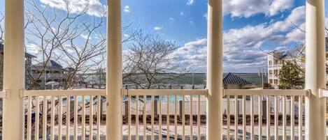 A covered porch with white columns and a view of a beach and buildings.