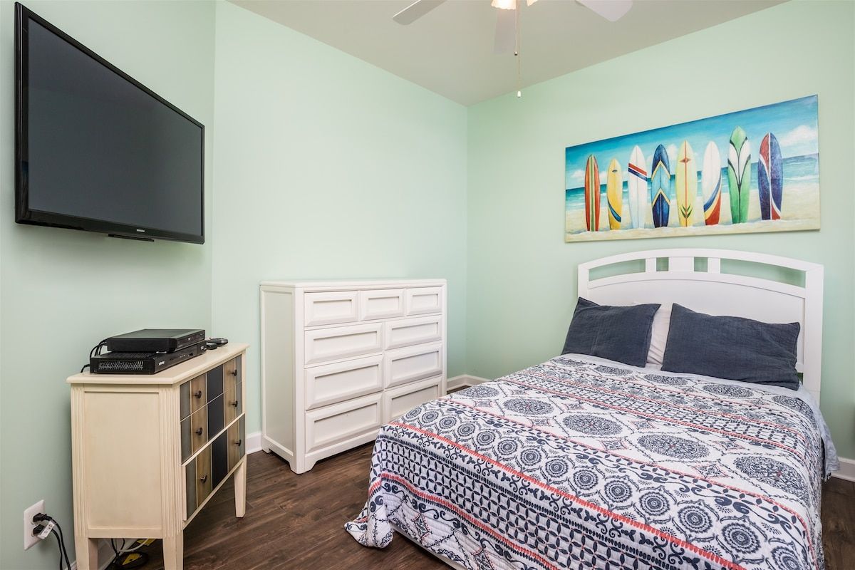 Un dormitorio con cama, cómoda, televisor y un cuadro en la pared.