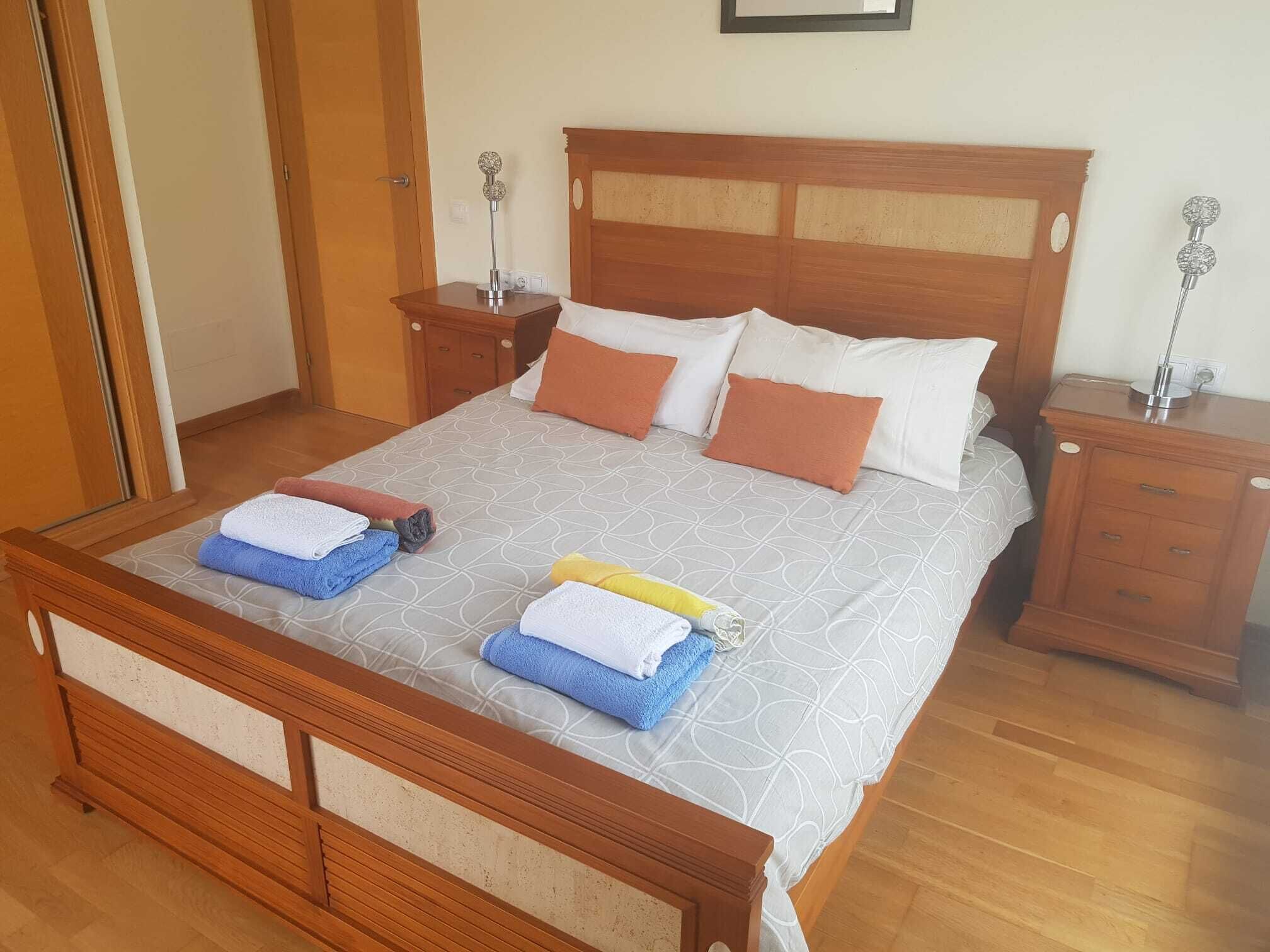 A neatly made bed with a wooden headboard, two bedside tables with lamps, and a wooden nightstand.