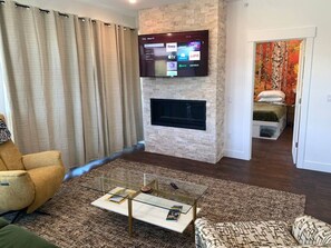 A living room with a fireplace, a flat-screen TV mounted above it, a sofa, a coffee table, and a patterned rug.