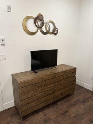Une commode en bois sur laquelle est posée une télévision à écran plat, une œuvre d’art abstraite accrochée au mur et un thermostat fixé au mur.
