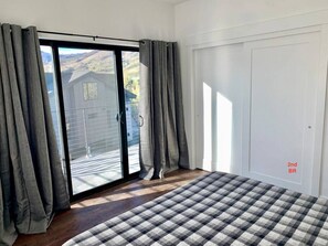 A bedroom with a large window, a sliding glass door, a checkered bedspread, and a white wardrobe.