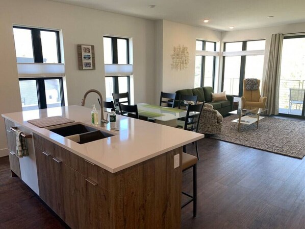 A modern kitchen with a central island, a dining area with a table and chairs, and a living area with a sofa and a chair.