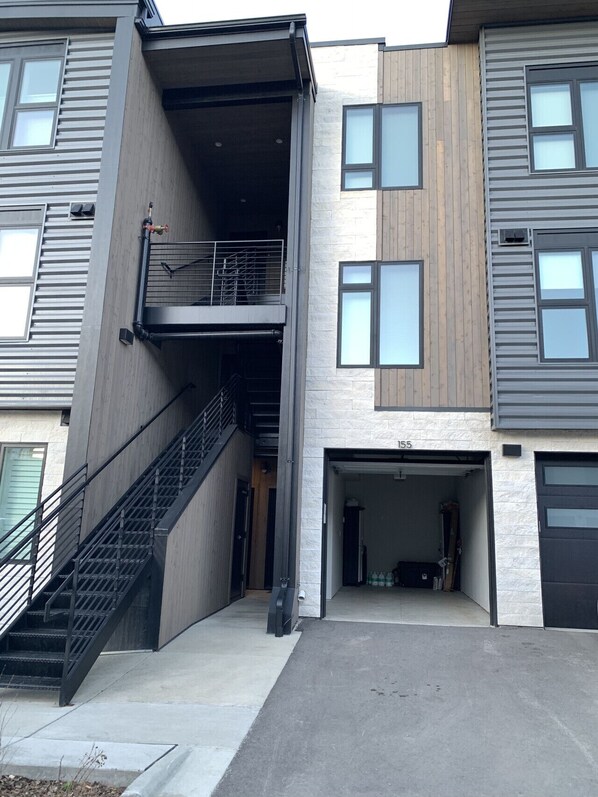 Un immeuble résidentiel moderne à plusieurs étages, doté d’un espace extérieur couvert, d’un escalier et d’un garage.