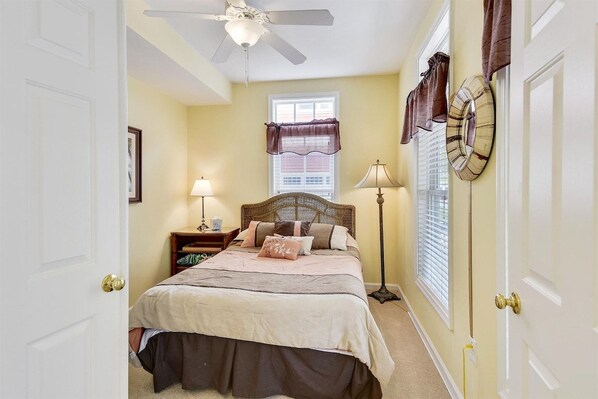 A bedroom with a bed, bedside lamps, a ceiling fan, a window with blinds, and a door with a doorknob.