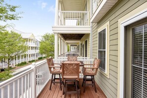 A wooden deck with a table and chairs, a white railing, and a building with a porch.