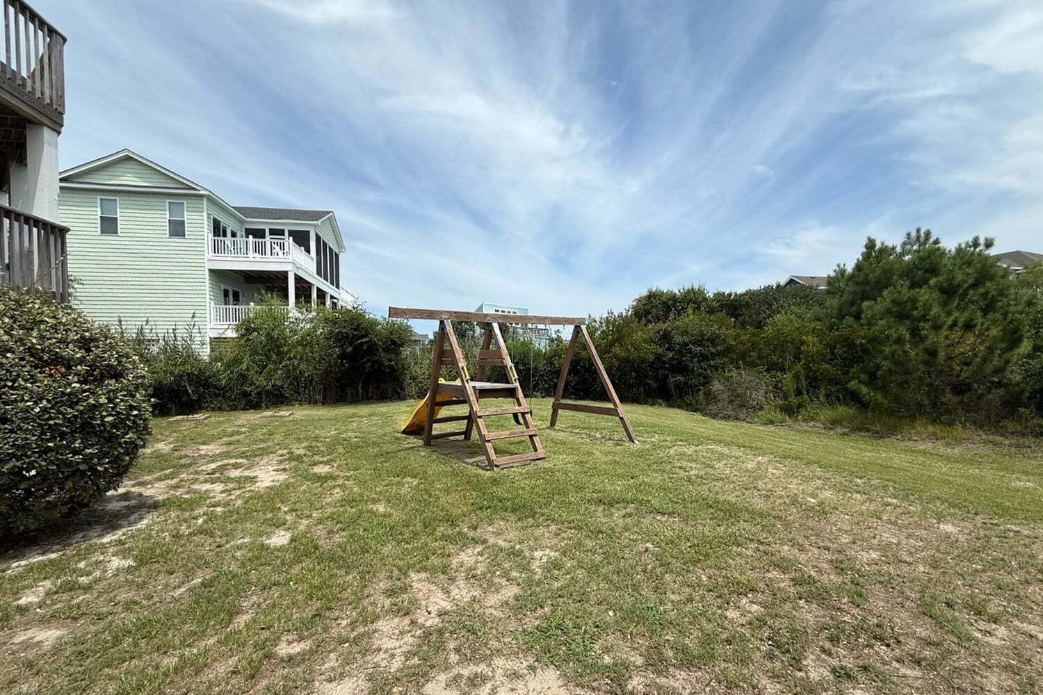 A grassy backyard with a wooden swing set and a slide.