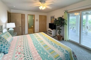 A bedroom with a bed, a TV, a plant, and a balcony with a view. - 1418 - Windswept - Walk to Beach | Pool, Hot Tub & Wraparound Deck (Corolla)