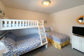 A room with bunk beds, a television, and a sun-shaped wall decoration. - 1418 - Windswept - Walk to Beach | Pool, Hot Tub & Wraparound Deck (Corolla)