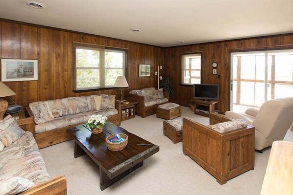 A wooden-paneled living room with a sofa, armchairs, a coffee table, and a television.