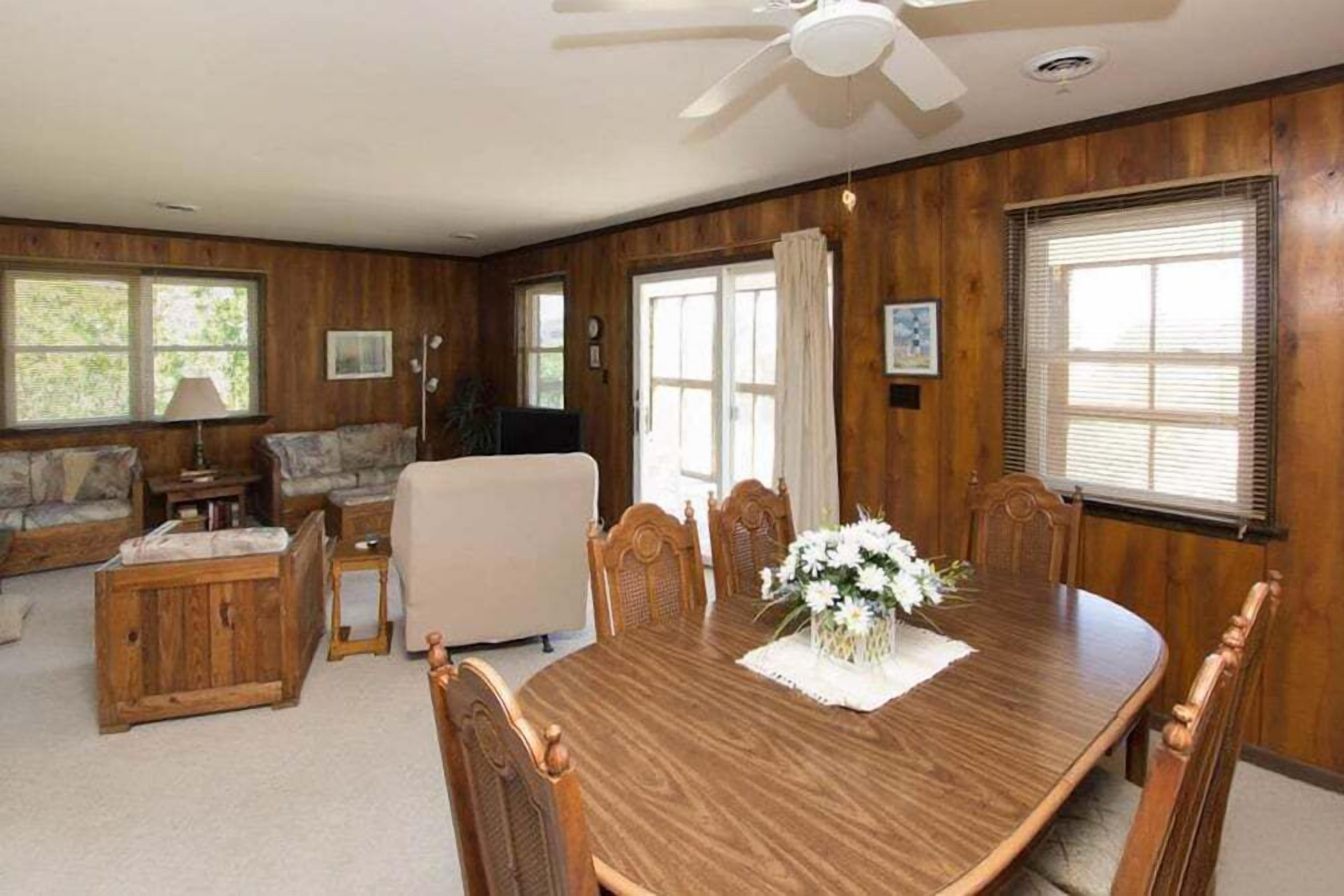 A spacious living room with a wooden dining table, comfortable seating, and large windows.