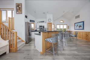 Une cuisine spacieuse dotée d’un îlot central, un coin repas avec des chaises en métal et un escalier menant à un autre niveau.