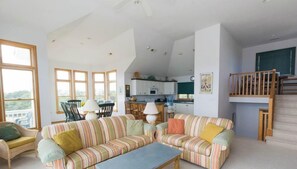 A spacious living area with a striped sofa, a dining table, and a kitchen in the background.